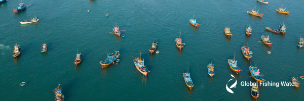 Aerial view of numerous colorful fishing boats scattered across blue-green water, with the Global Fishing Watch logo in the lower right corner.
