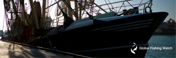 A docked fishing vessel in partial shadow with fishing nets visible, water and industrial structures in the background. The Global Fishing Watch logo appears in the lower right corner.