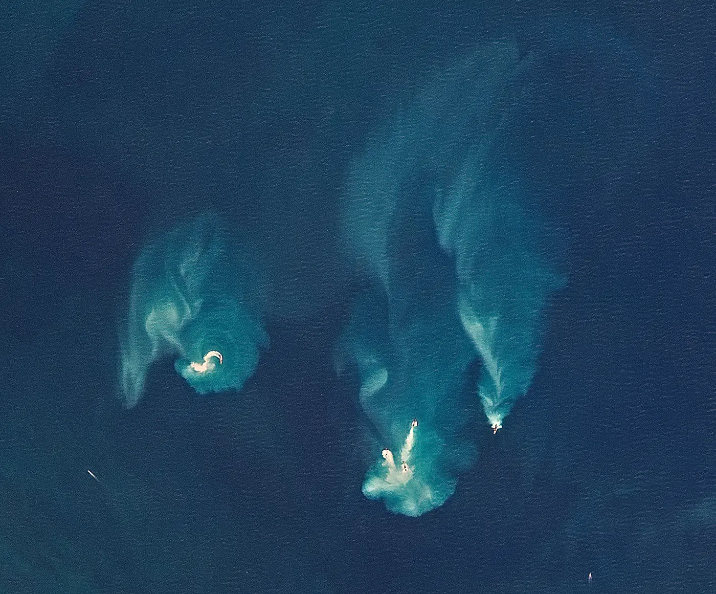 Una vista por satélite del océano muestra dos pequeñas islas y remolinos de agua azul verdosa, probablemente causados por actividad volcánica submarina o arrecifes poco profundos, rodeados de un mar azul profundo.