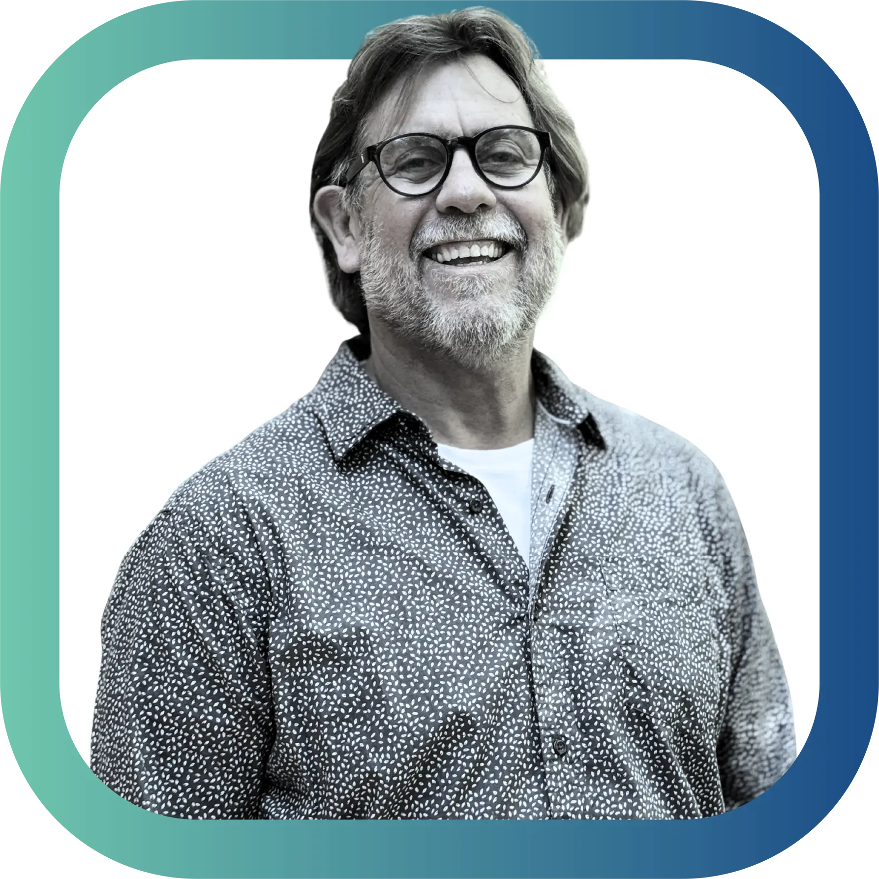 Un hombre sonriente de mediana edad con gafas, barba y camisa estampada aparece sobre un fondo blanco, enmarcado por un borde redondeado azul y verde.