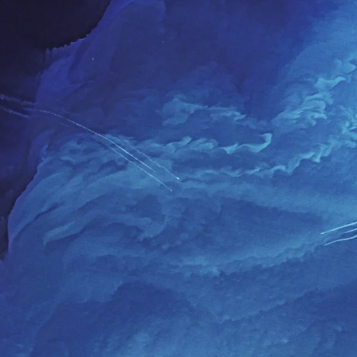 Satellite ocean image in shades of blue with swirling patterns and several thin, white boat wake lines curving across the surface.