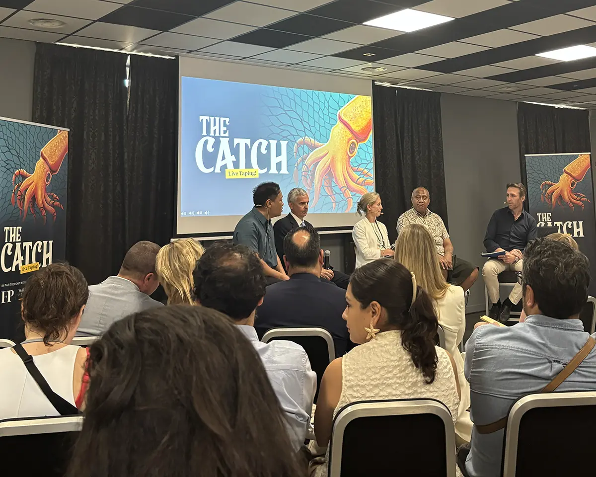 Un panel de six personnes est assis à l'avant d'une salle, discutant de The Catch devant un public. Derrière eux, des bannières et un écran affichent le titre avec l'illustration d'un calmar.